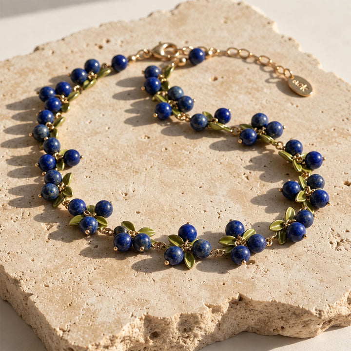 Natural lapis lazuli berry necklace with green enamel leaves displayed on textured limestone in sunlight
