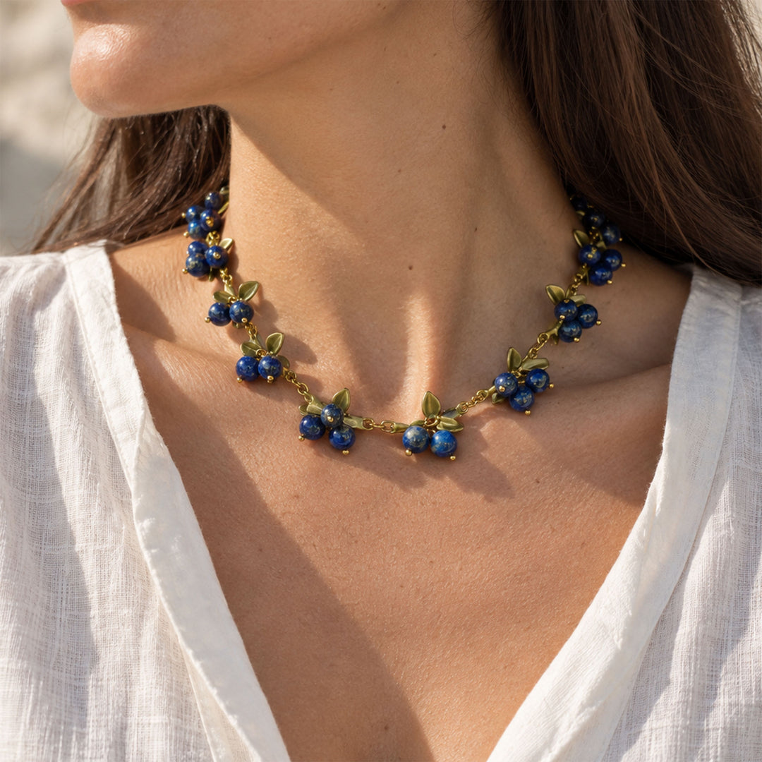 Model wearing Lapis Lazuli Berry Garden Necklace with blue gemstone clusters and hand-painted green enamel leaves
