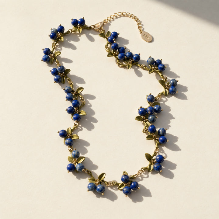 Lapis Lazuli Berry Garden Necklace with hand-painted green enamel leaves and gold-plated details on a light surface