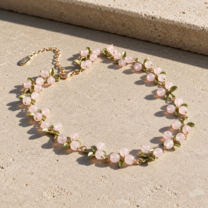 Rose quartz Berry Garden Necklace with green enamel leaves and gold-plated details in sunlight