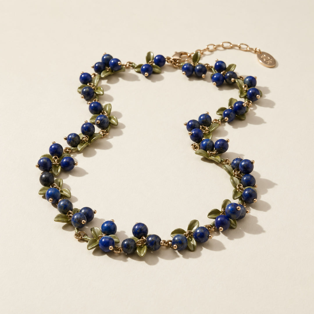 Lapis Lazuli Berry Garden Necklace with hand-painted green enamel leaves and gold-plated details on a light surface