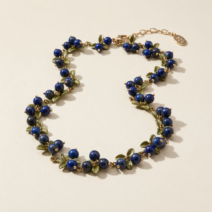 Lapis Lazuli Berry Garden Necklace with hand-painted green enamel leaves and gold-plated details on a light surface