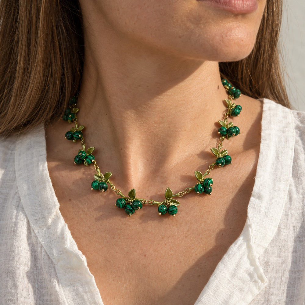 A close-up of a woman wearing a Malachite Berry Garden Necklace with natural green gemstone clusters and enamel leaf details, paired with a white blouse.