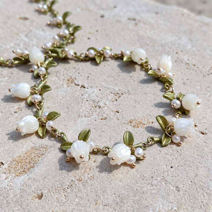 Close-up of a MOP Lily of the Valley necklace with hand-carved mother-of-pearl flowers, freshwater pearls and green enamel leaves on stone surface.