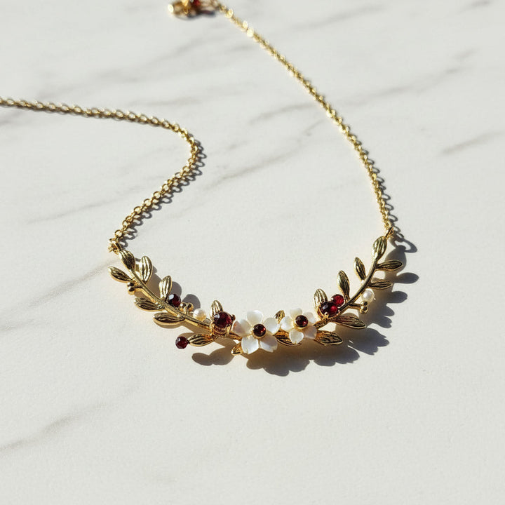 Gold necklace with leaf design and embedded stones on a light background