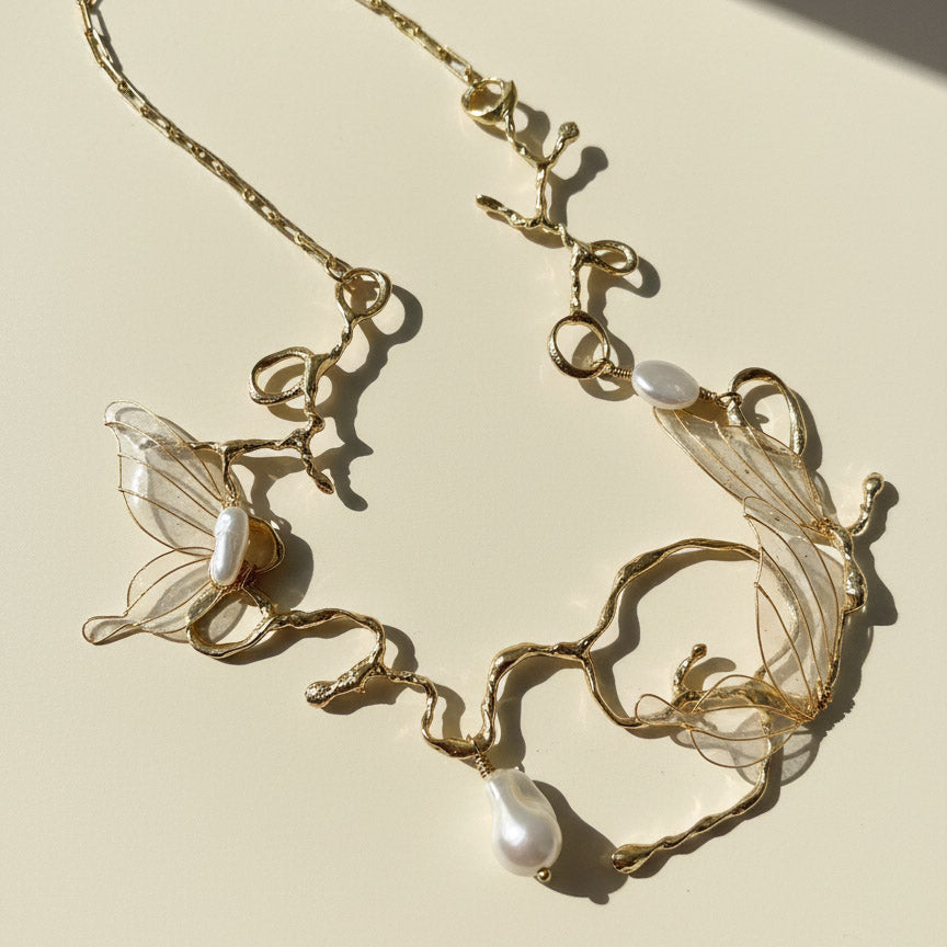 Gold necklace with butterfly and pearl designs on a beige background
