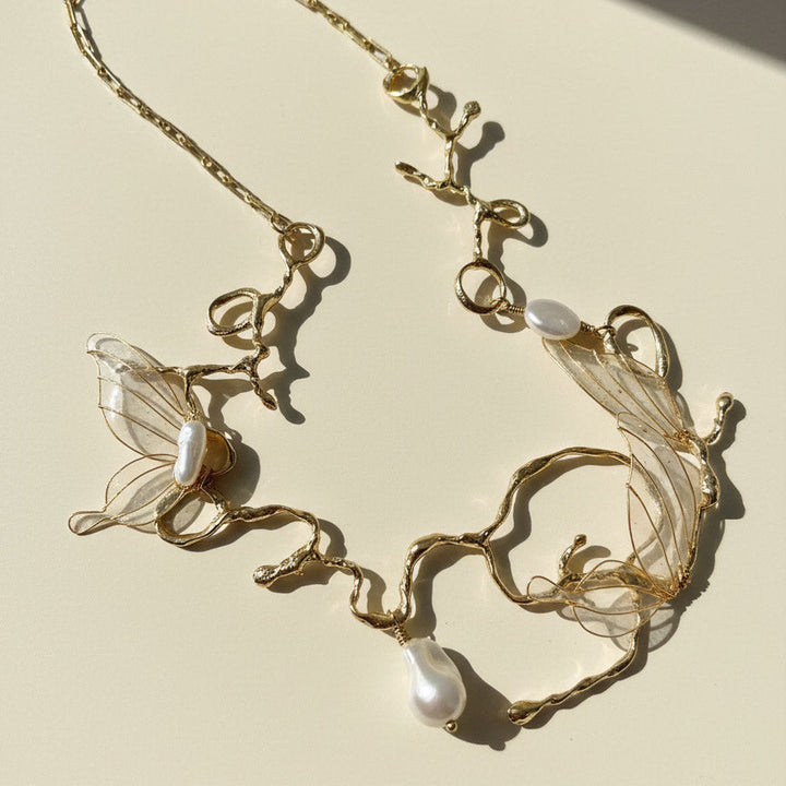 Gold necklace with butterfly and pearl designs on a beige background