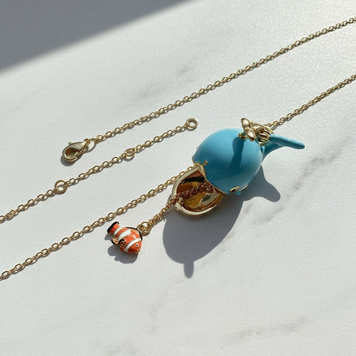 Necklace with a blue whale pendant and orange fish charm on a light background