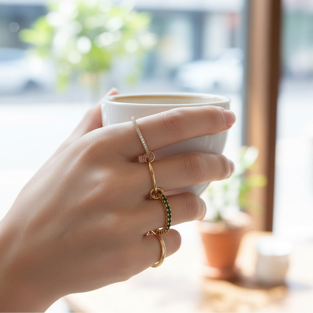 Hand holding a white mug with gold rings on fingers, blurred indoor background