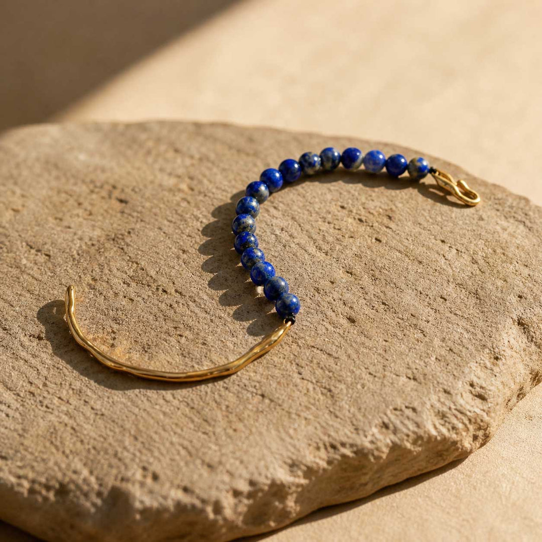 Lapis lazuli bracelet styled on natural beige stone slab with gold hook detail