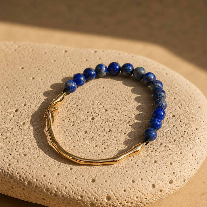 Lapis lazuli beaded bracelet with gold hook clasp on textured stone surface