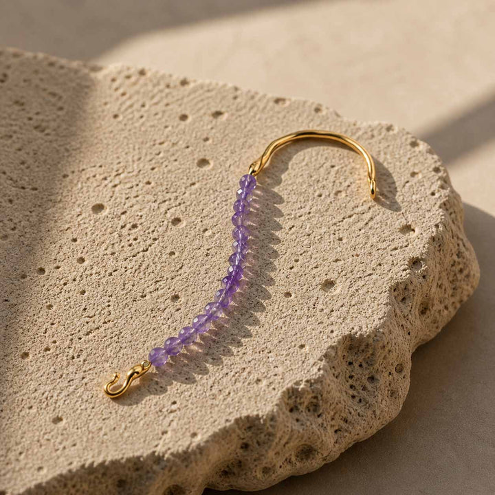 Amethyst gemstone hook bracelet with gold plated stainless steel details on textured stone surface