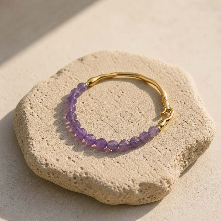 Amethyst and gold hook bracelet styled on natural beige stone slab