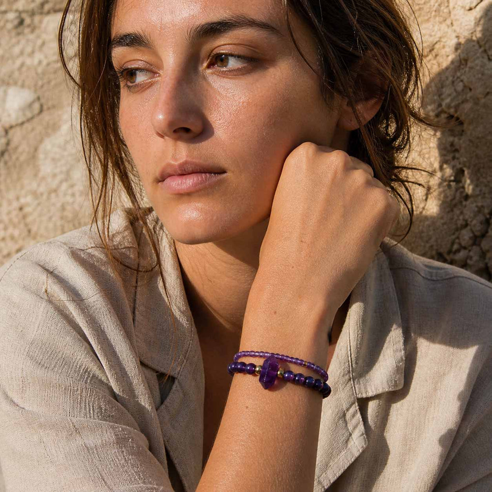 Woman wearing layered amethyst gemstone bracelets with gold details