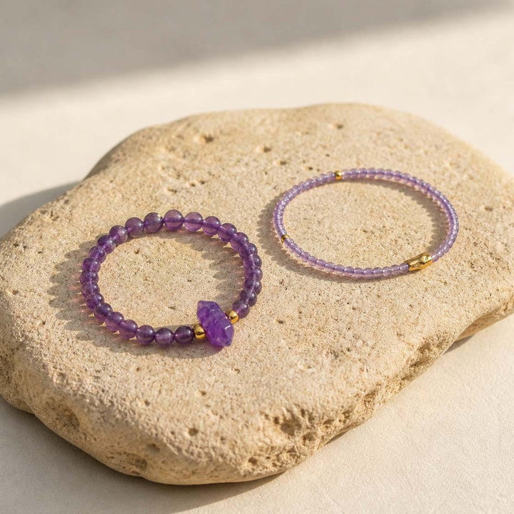Amethyst bracelet stack styled on textured beige stone slab