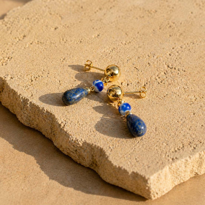 Lapis lazuli and porcelain drop earrings on textured beige stone surface