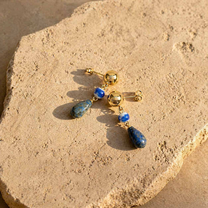 Blue lapis lazuli drop earrings styled on natural stone slab with gold stainless steel finish