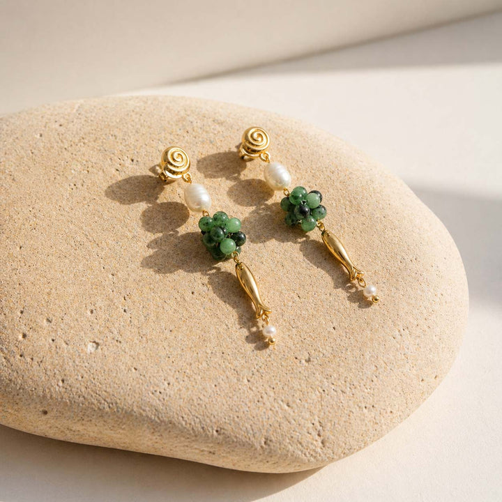 Ruby zoisite and pearl drop earrings on natural beige stone surface