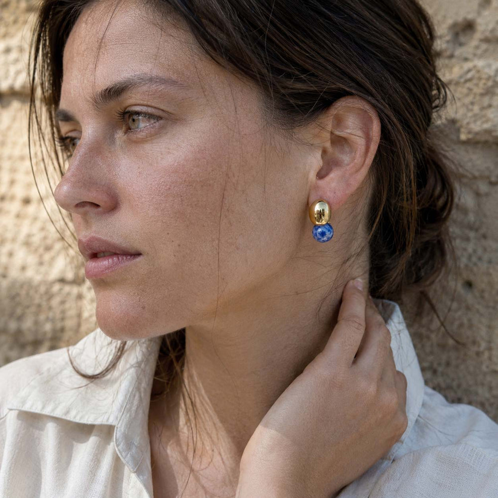 Woman wearing Sodalite sculptural ball earrings against a stone wall background