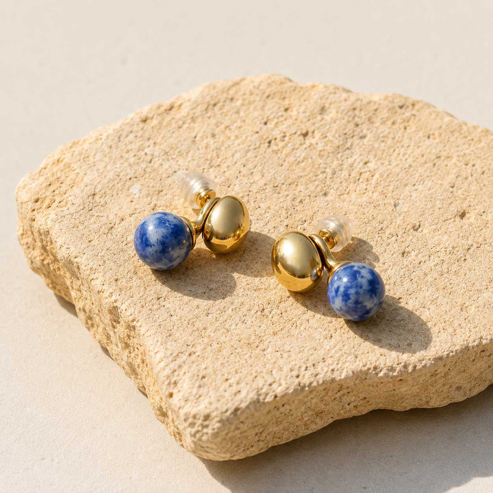 Sodalite sculptural ball earrings on terracotta stone on a beige stone surface