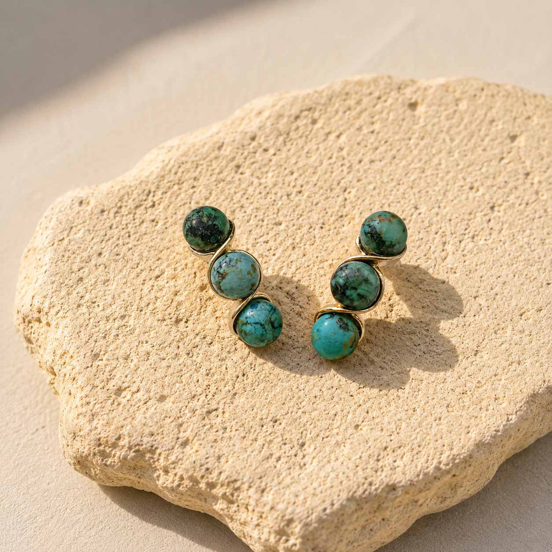 Turquoise stone earrings on a textured beige surface