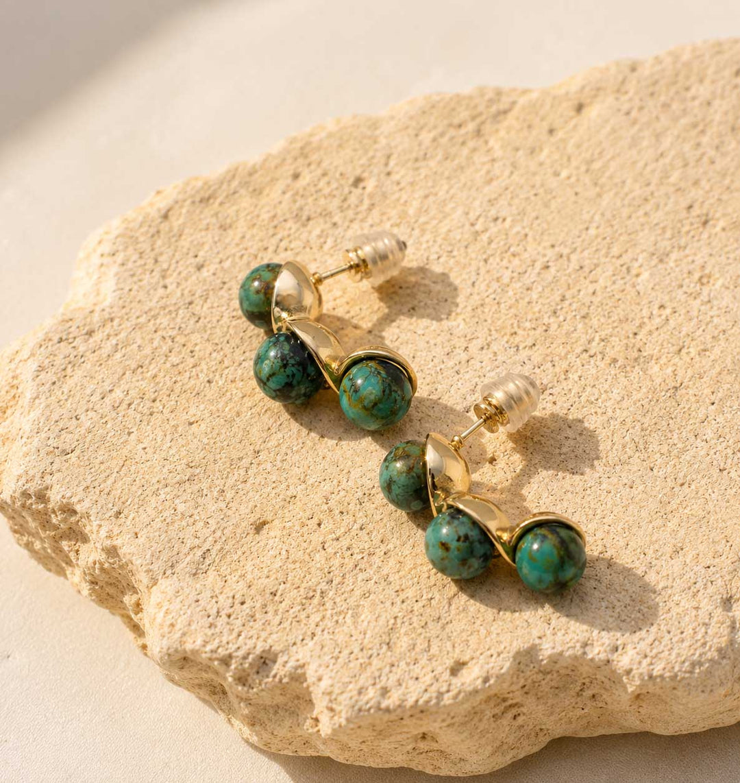 Gold and turquoise beaded earrings on a textured stone surface