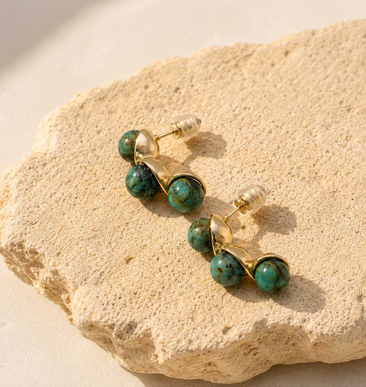 Gold and turquoise beaded earrings on a textured stone surface