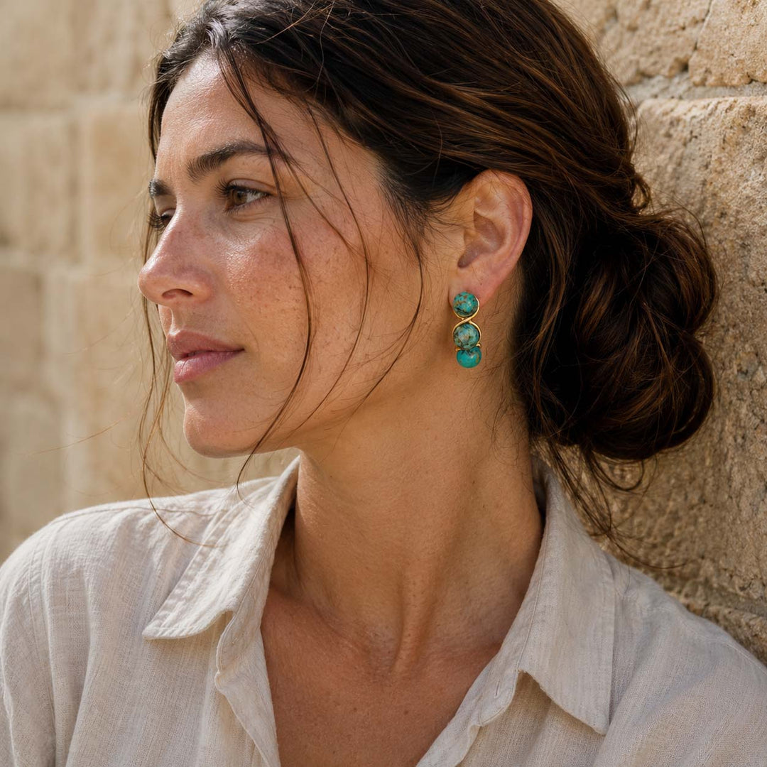 Woman wearing African Turquoise triple bead earrings against a stone wall