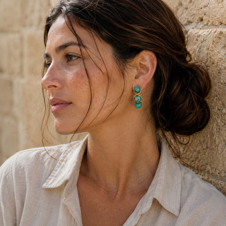 Woman wearing African Turquoise triple bead earrings against a stone wall