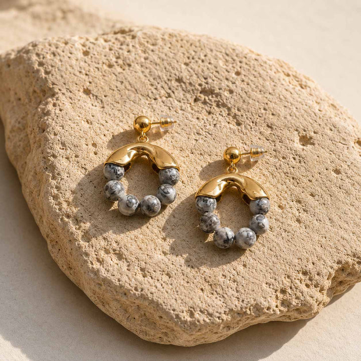 Gold beaded hoop earrings with gray Map Jasper stones on textured stone