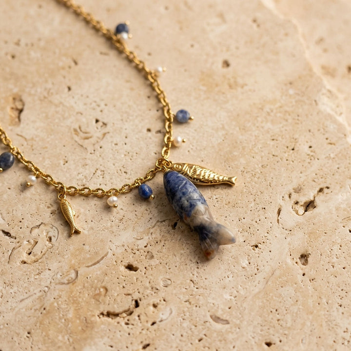 Gold necklace with hand-carved sodalite fish pendant and pearl accents on textured stone