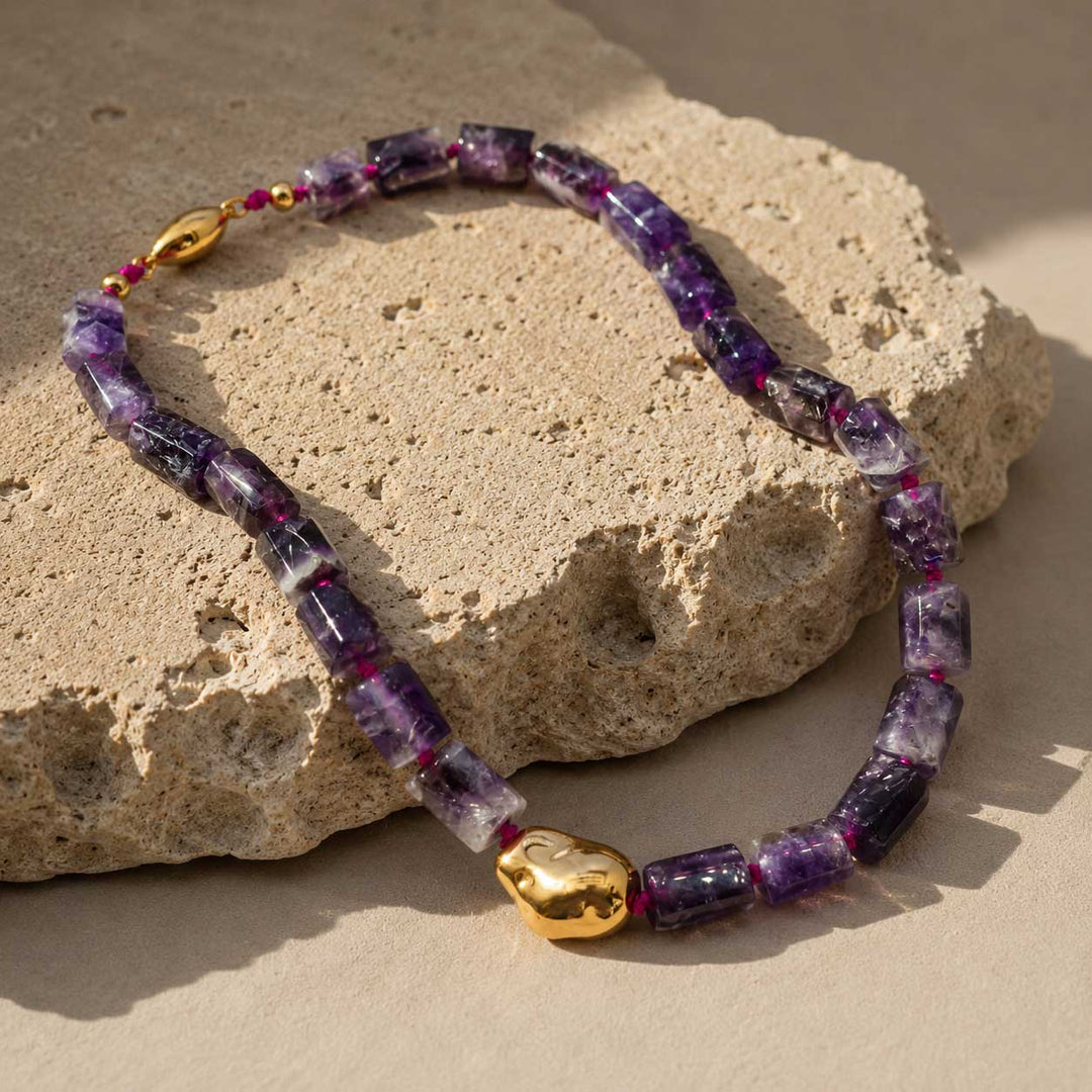 A2K London handcrafted amethyst sculptural necklace displayed on natural limestone, featuring faceted amethyst gemstone beads and a gold PVD stainless steel accent.