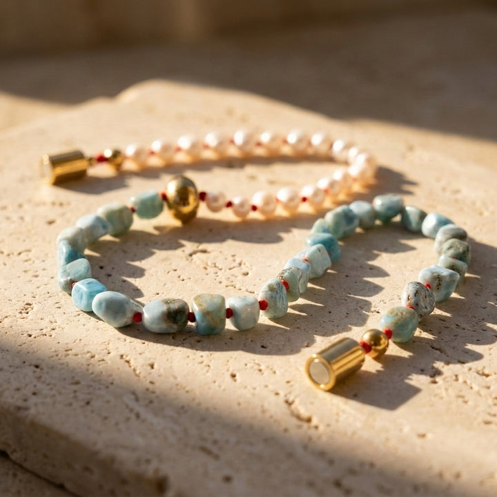 Larimar and freshwater pearl necklace with red hand-knotted details and gold magnetic clasp in warm natural sunlight.