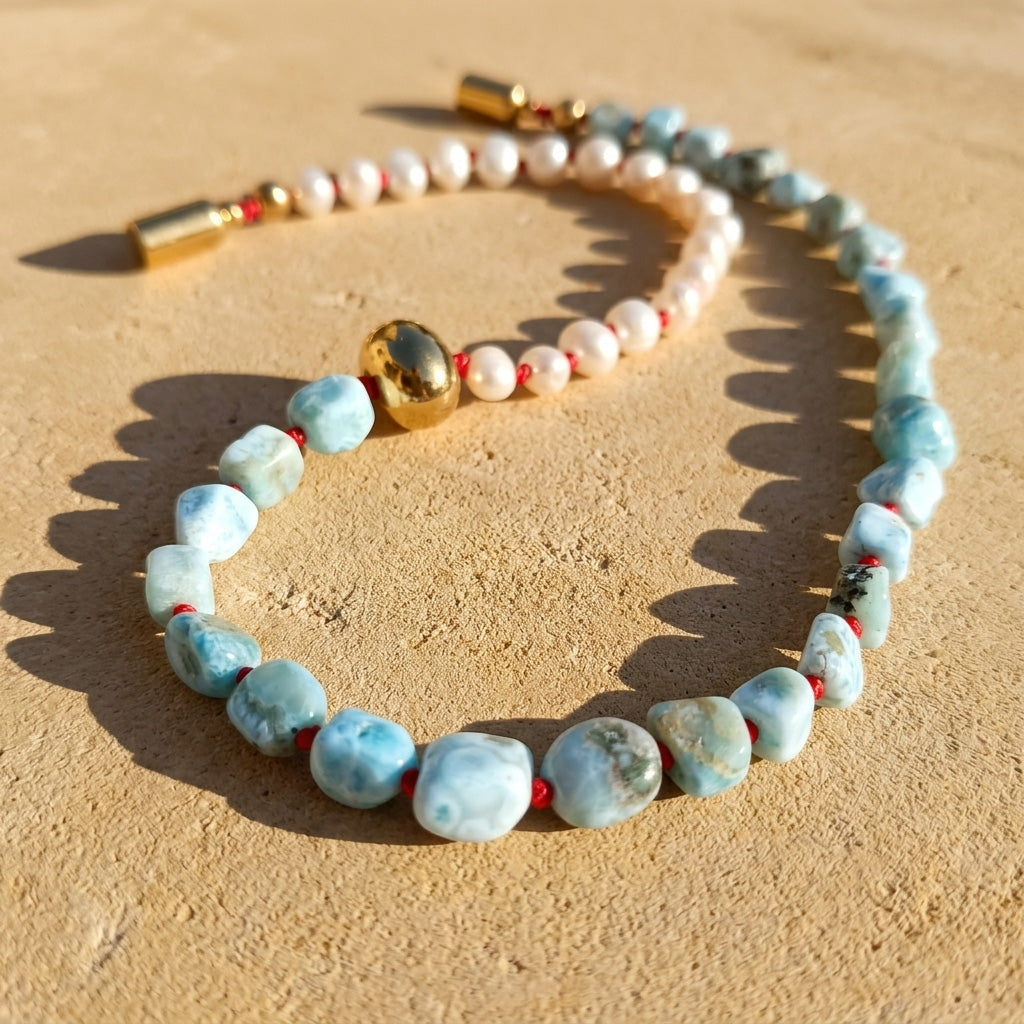 Larimar pearl necklace arranged on a light stone surface with natural blue gemstone beads and gold magnetic clasp, displayed on a sandy beige surface.