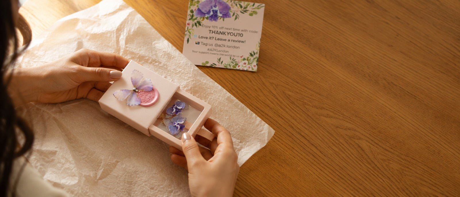 Hands opening an A2K London gift box with butterfly earrings and a thank you card